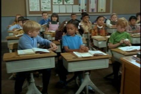 While the teacher's back is turned, Jody is fondling a baseball, which his friend Peter wants to see.