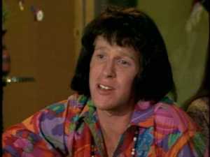 "I'm living, baby!" he exclaims from beneath an unfortunate wig.